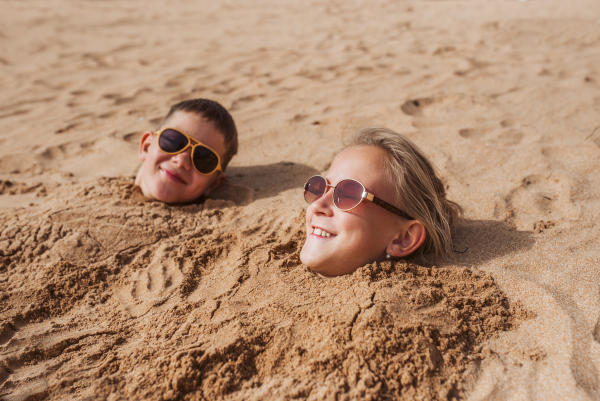 Children buried in sand on the beach, having fun during a family vacation.