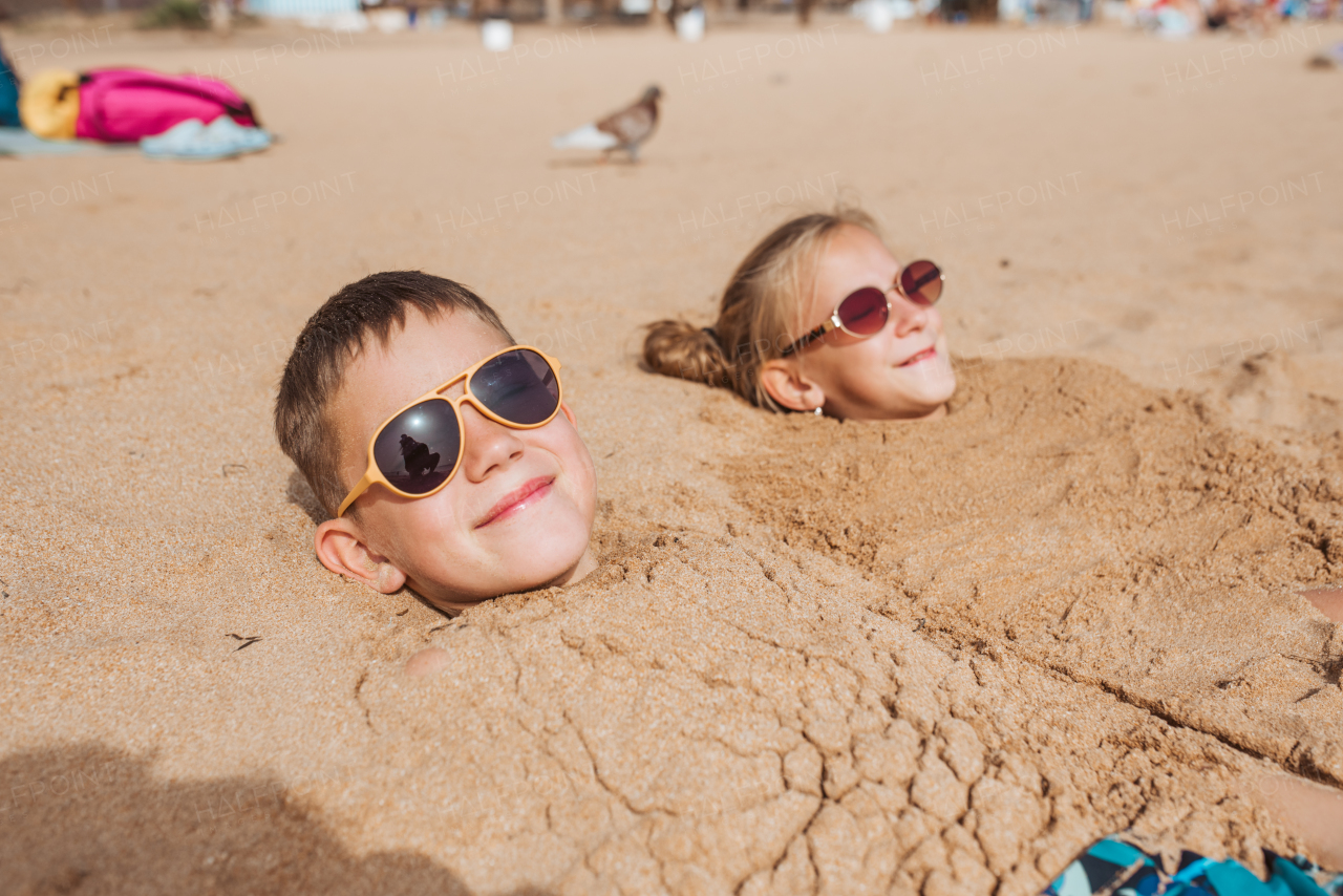 Children buried in sand on the beach, having fun during a family vacation.