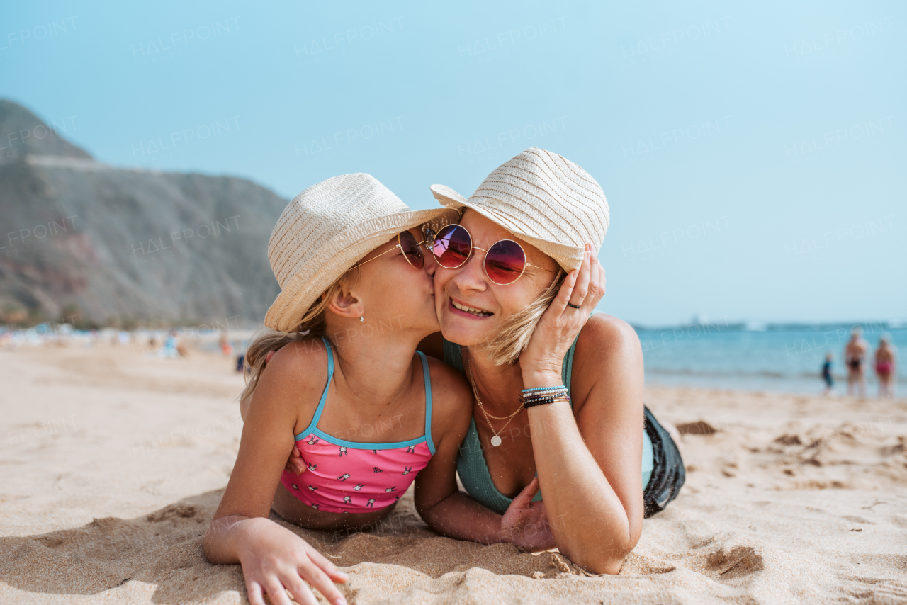 Portrait of mother and daughter on sandy beach, wearing hats and sunglasses.