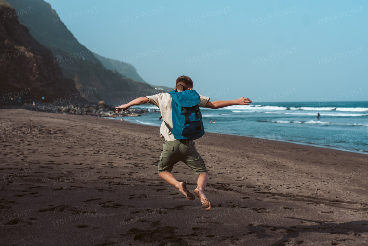 Boy is excited to be on a family vacation, jumping on the beach.