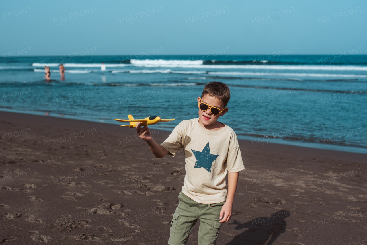 Boy playing on a sandy beach with a foam airplane.