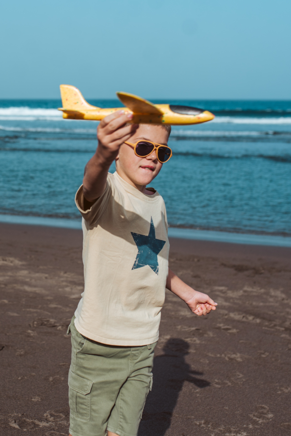 Boy playing on a sandy beach with a foam airplane.