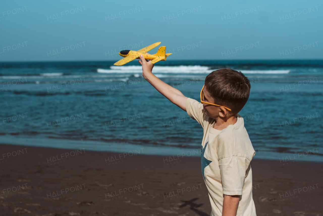 Boy playing on a sandy beach with a foam airplane.