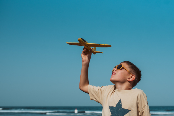 Boy playing on a sandy beach with a foam airplane.