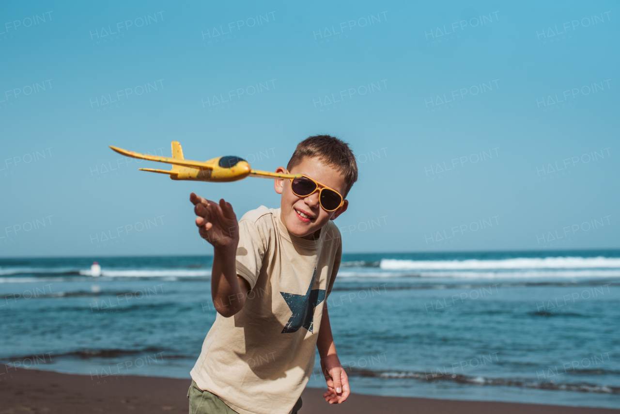 Boy playing on a sandy beach with a foam airplane.