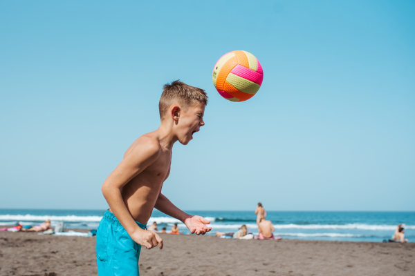 Young boy playing soccer on a sandy beach, enjoying a family vacation.