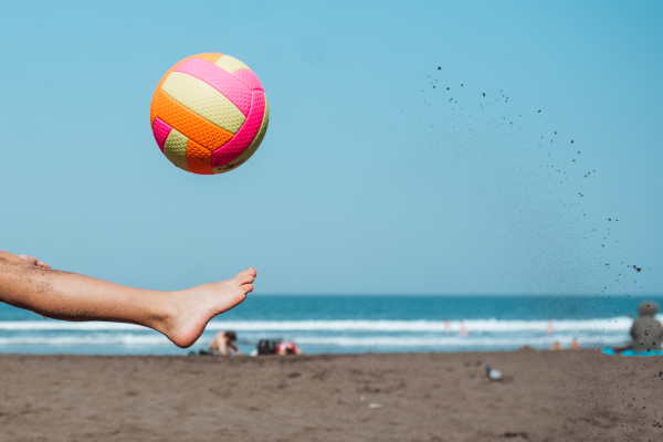 Close up of boy's leg kicking soccer on a sandy beach, enjoying a family vacation.