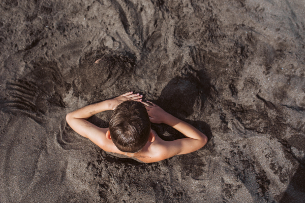 Top view of boy buried in sand on the beach, having fun during a family vacation.