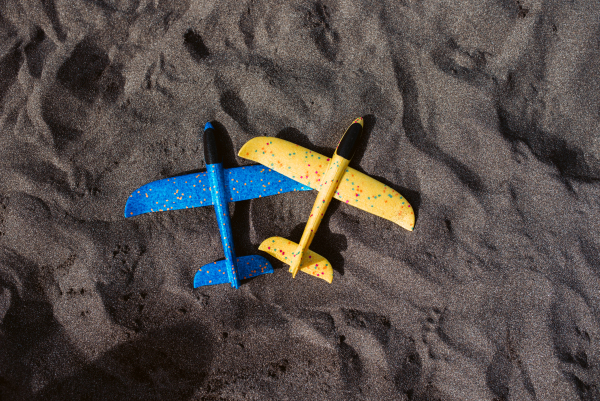 Two foam gliders on the sand beach. Blue and yellow toy airplanes.