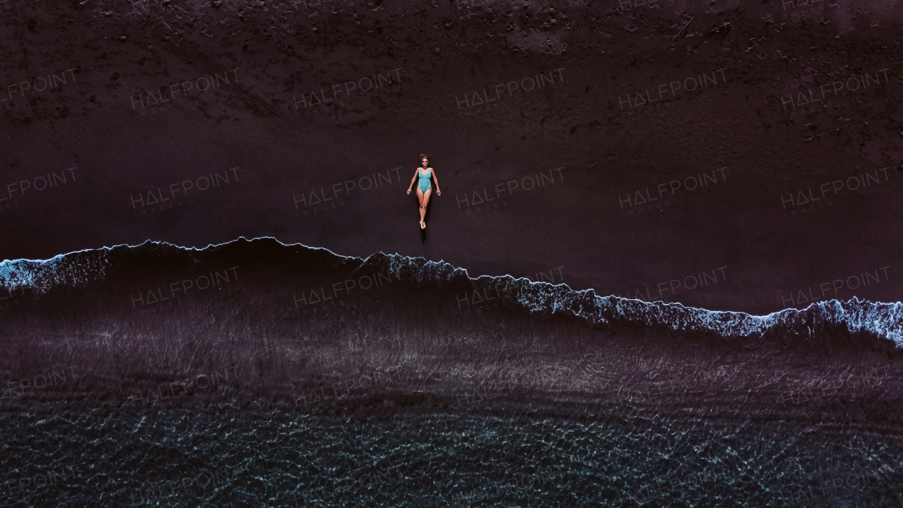 Aerial view of woman lying on a sandy beach near the water.