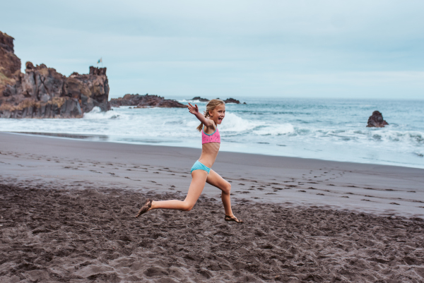 Rear view of girl running across the beach into sea. Concept of family beach summer vacation with kids.