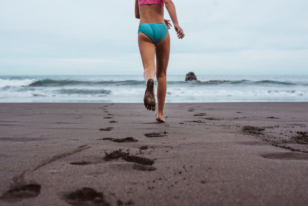 Rear view of girl running across the beach into sea. Concept of family beach summer vacation with kids.