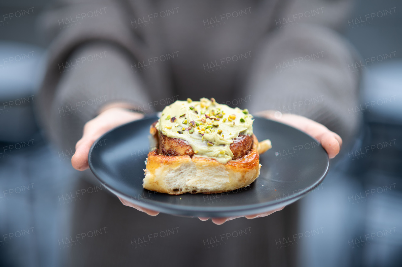 Close up of hands holding plate with pistachio cinnamon bun.