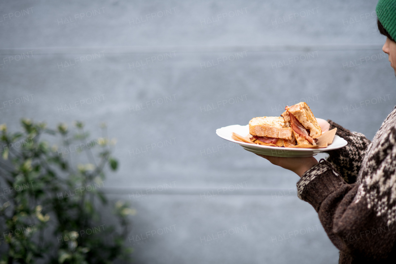 Girl holding plate with homemade baked bacon sandwich. Gray background with copy space.