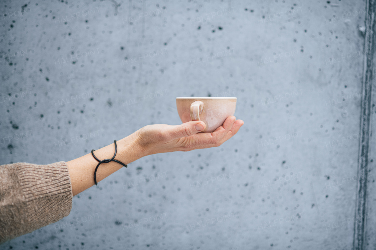 Close up of hand holding cup with coffee in front of gray concrete wall.