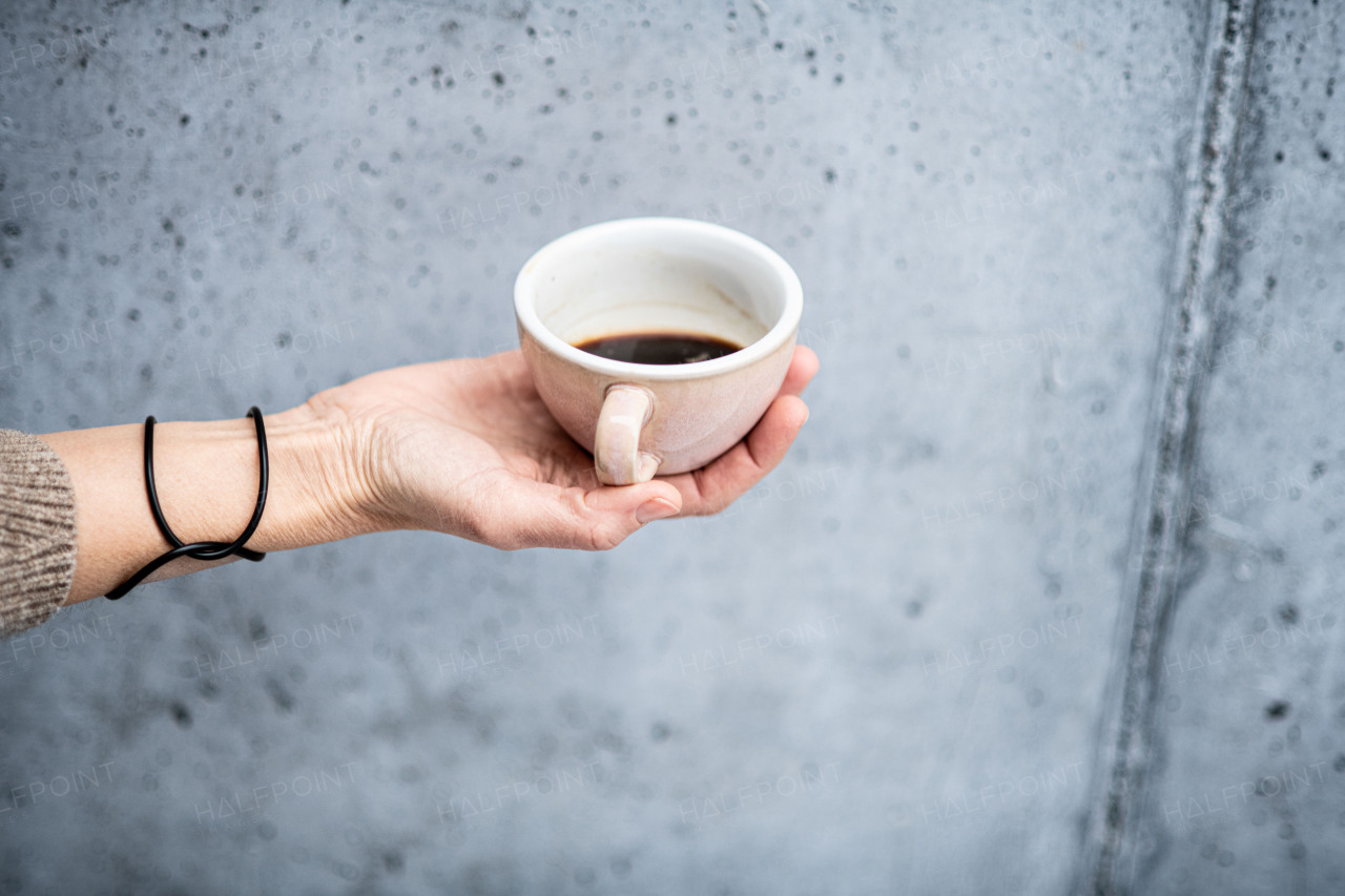 Close up of hand holding cup with coffee in front of gray concrete wall.