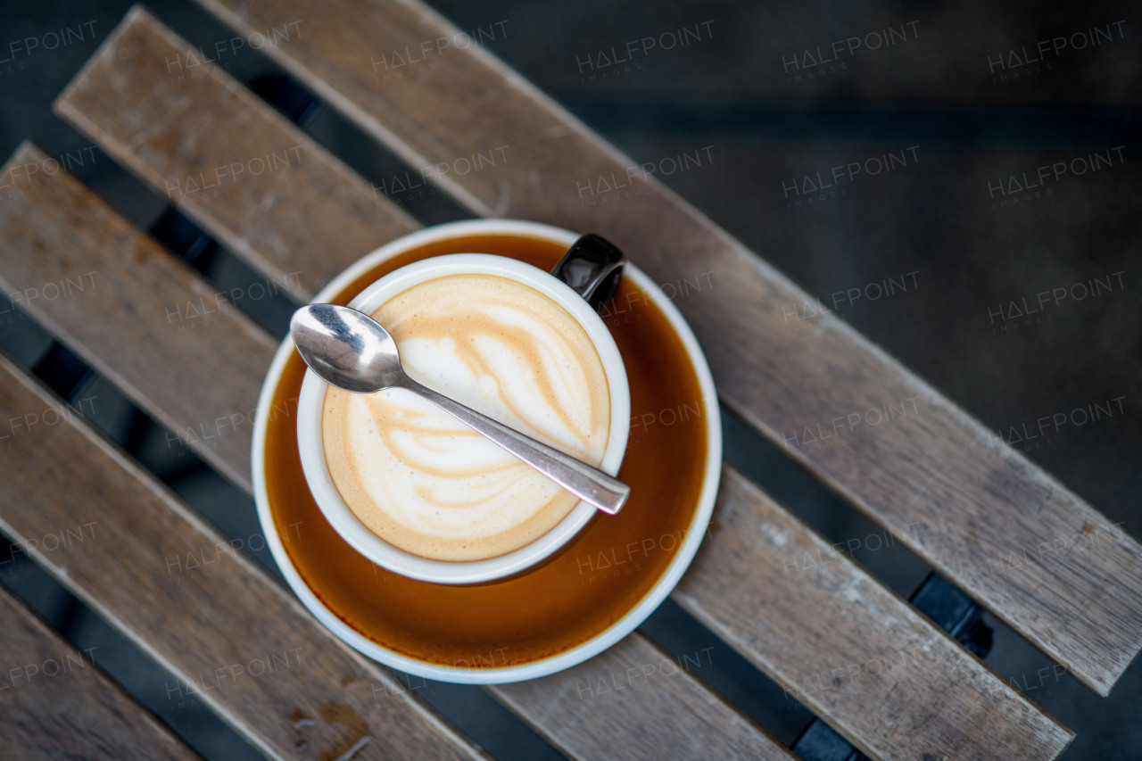 Top view of cup of cappuccino with latte art on a rustic wooden table in a cozy cafe setting.