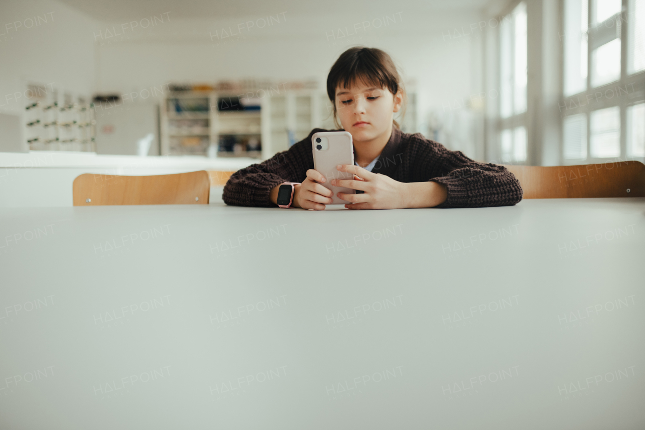 Young schoolgirl sitting in a science lab with a phone in her hand, waiting for classmates. Cyberbullying at school.