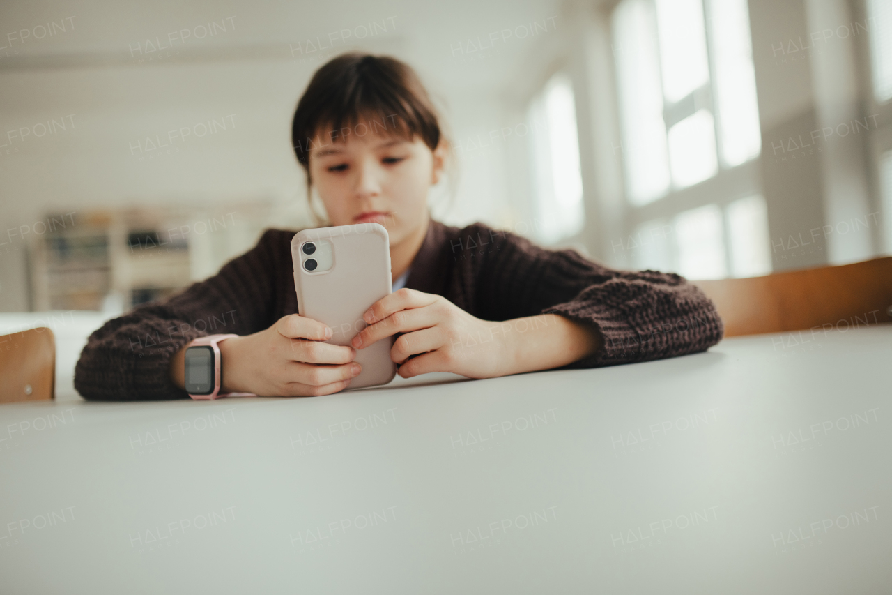 Young schoolgirl sitting in a science lab with a phone in her hand, waiting for classmates. Cyberbullying at school.