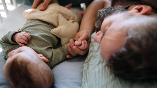 Father cosleeping with baby boy, lying in bed and holding hands.