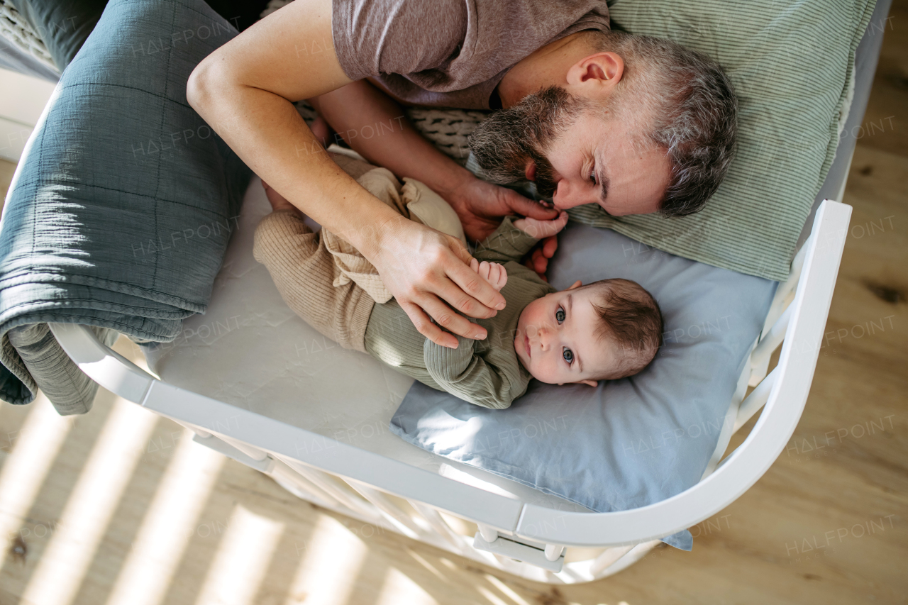 Father putting the baby to sleep, lying next to him in the crib and soothing him.