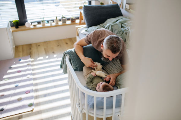 Father putting the baby to sleep, lying next to him in the crib and soothing him.