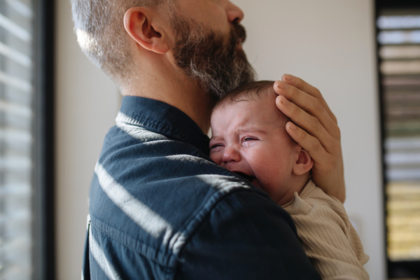 Father comforting his crying baby son, holding him in arms.