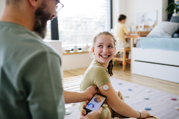 Diabetic girl with a CGM sensor on her arm. Father using an app to monitor blood sugar levels.