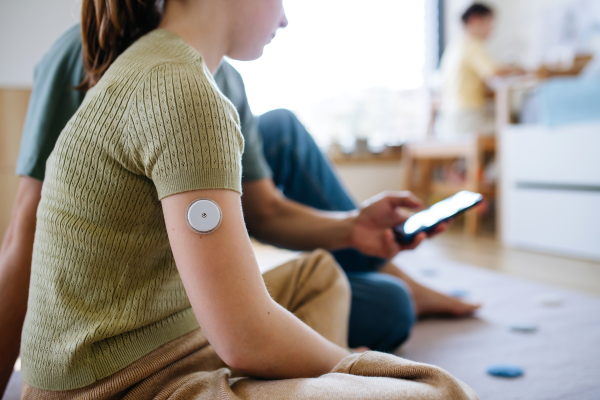 Diabetic girl with a CGM sensor on her arm. Father using an app to monitor blood sugar levels.