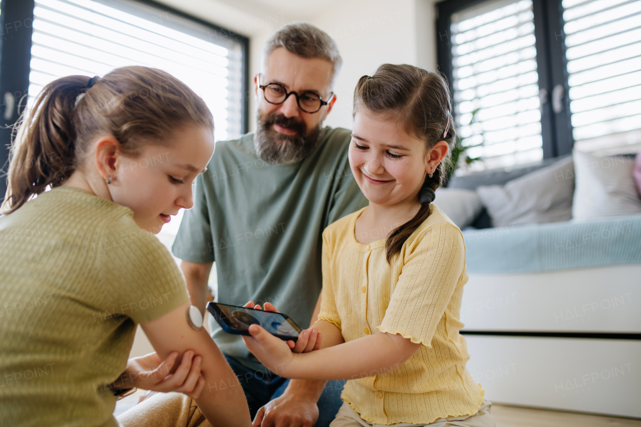 Diabetic girl with a CGM sensor on her arm. Sister learning how to use app to monitor blood sugar levels.