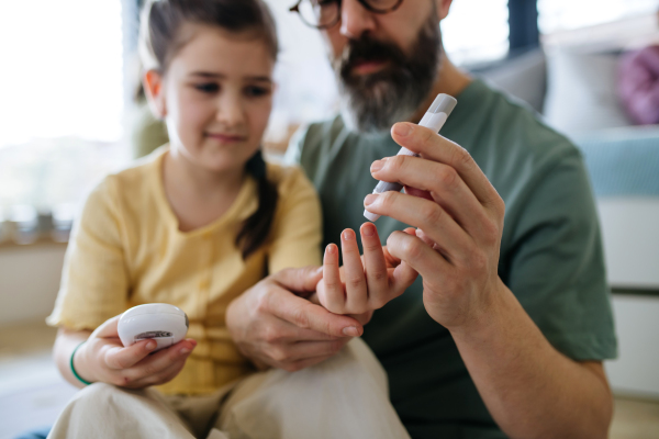 Father assisting his daughter with a blood sugar test at home.