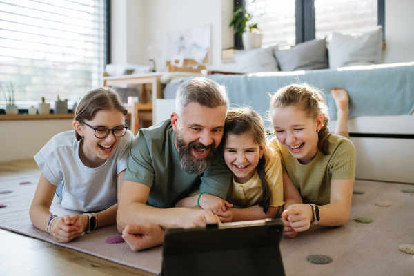 Portrait of father with three daughters watching tv show on tablet. Girl dad concept.