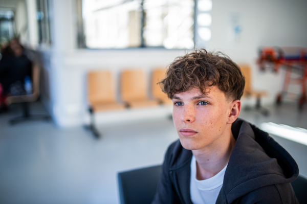 Teenage boy waiting alone in hospital waiting area before preventive medical checkup.