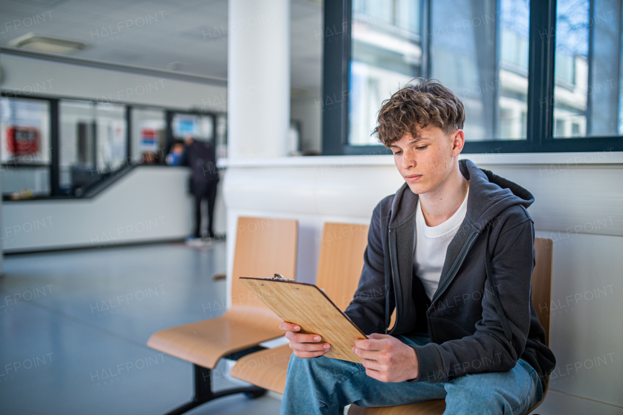 Teenage patient filling out medical forms in hospital hallway before examination. Hospital setting.