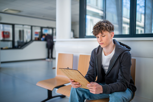 Teenage patient filling out medical forms in hospital hallway before examination. Hospital setting.