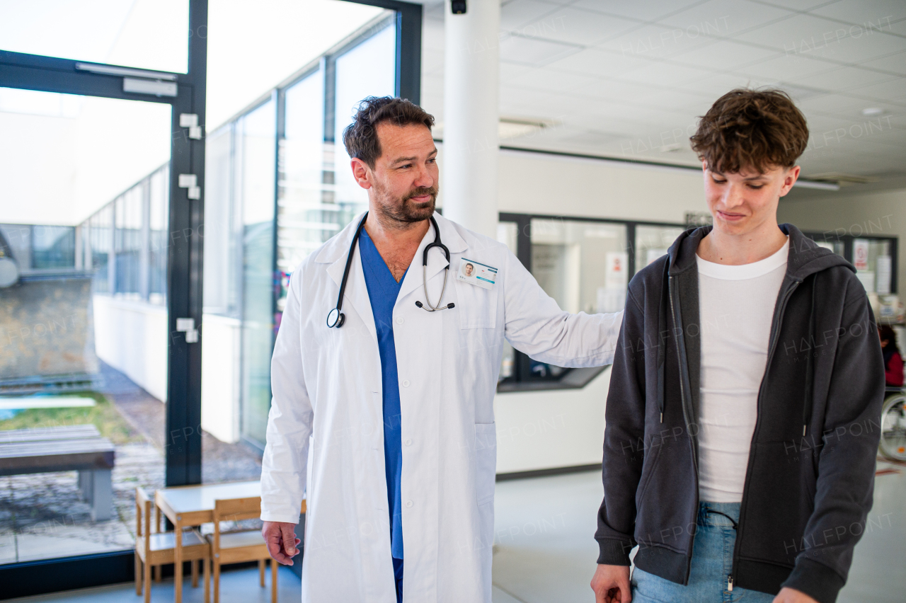 Doctor walking with teenage patient after successful checkup or medical procedure in hospital hallway.