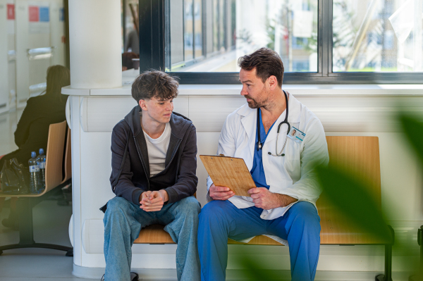 Doctor talking with teenage patient in modern hospital waiting room.