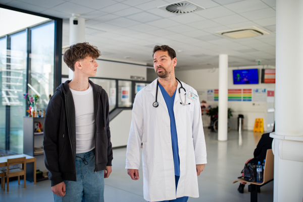 Doctor walking with teenage patient down the hospital hallway. Modern medical clinic.