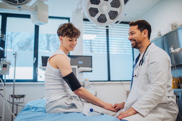 Teen boy undergoing medical checkup with smiling doctor in hospital room.