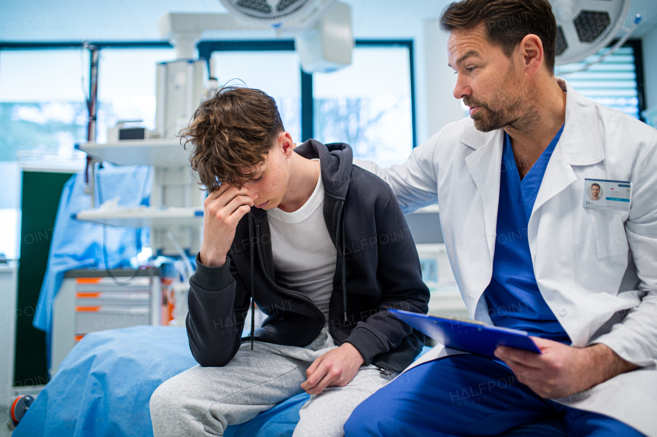 Depressed teenage boy patient sitting on hospital bed, talking with caring doctor.