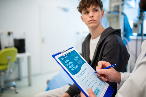 Close-up of doctor and teenage patient filling out mental health evaluation form together.