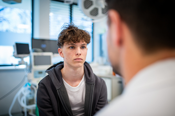 Depressed teenage boy patient sitting on hospital bed, talking with caring doctor.
