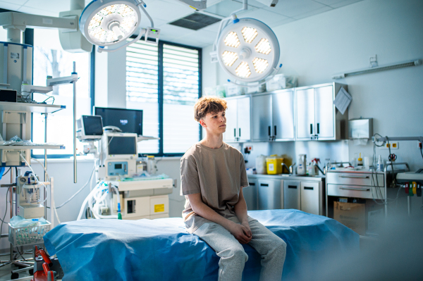 Teenage boy patient sitting on examination table in hospital, waiting for doctor.