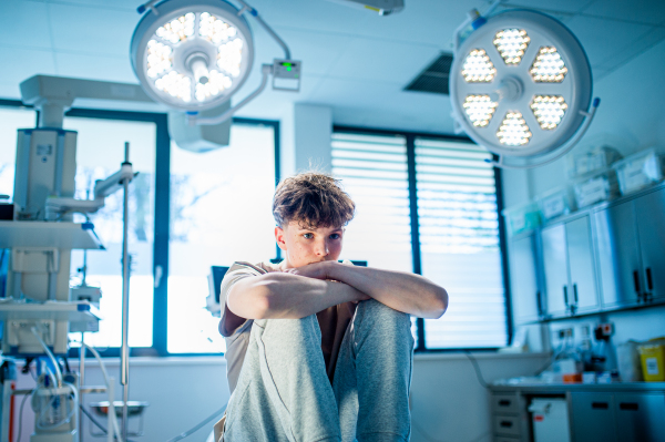 Teenage boy patient sitting on examination table in hospital, waiting for doctor.