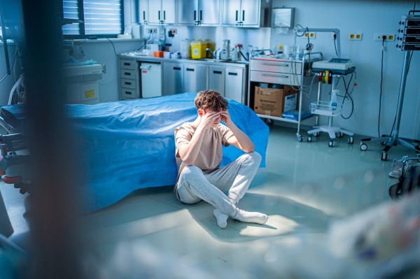 Worried teenage patient sitting alone on hospital floor, struggling with mental health issues and anxiety.