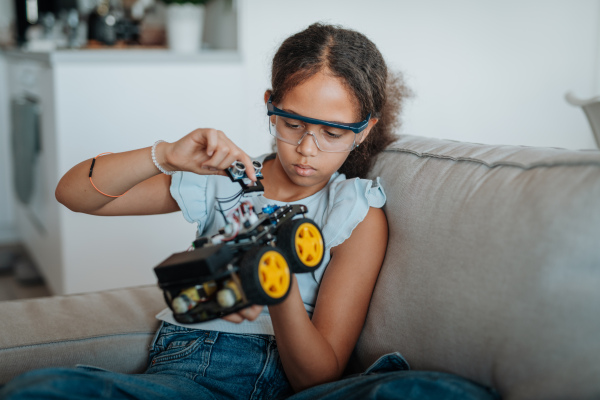 Focused girl building and programming robot car at home as part of STEM learning.