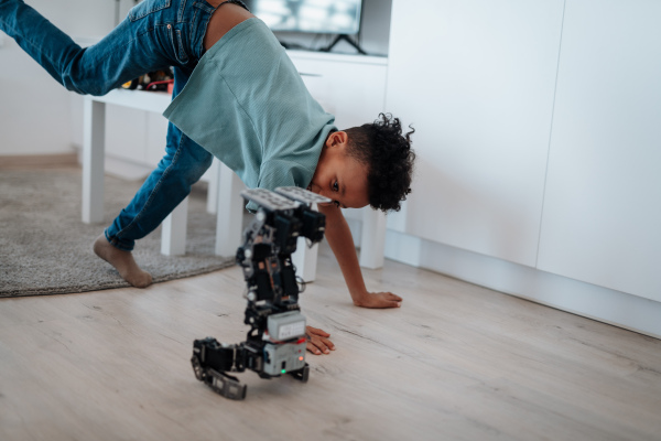 Cute boy having fun with small robot at home as part of STEM learning.