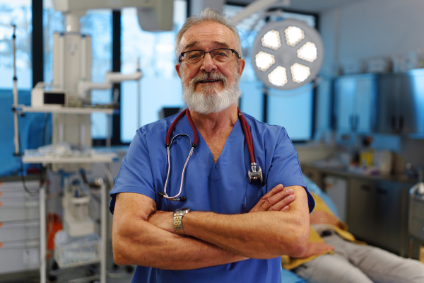 Portrait of older doctor standing in examination room in hospital.