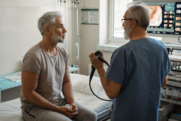 Doctor explaining colonoscopy results to patient using monitor images on screen.