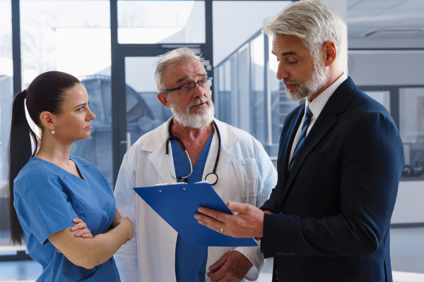Medical sales representative presenting new medication to doctors, standing hospital hallway. Hospital setting.
